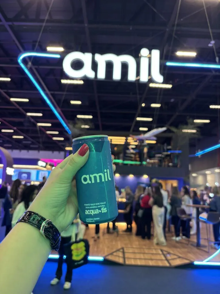 Lata personalizada da Amil na mão, com o letreiro do estande ao fundo