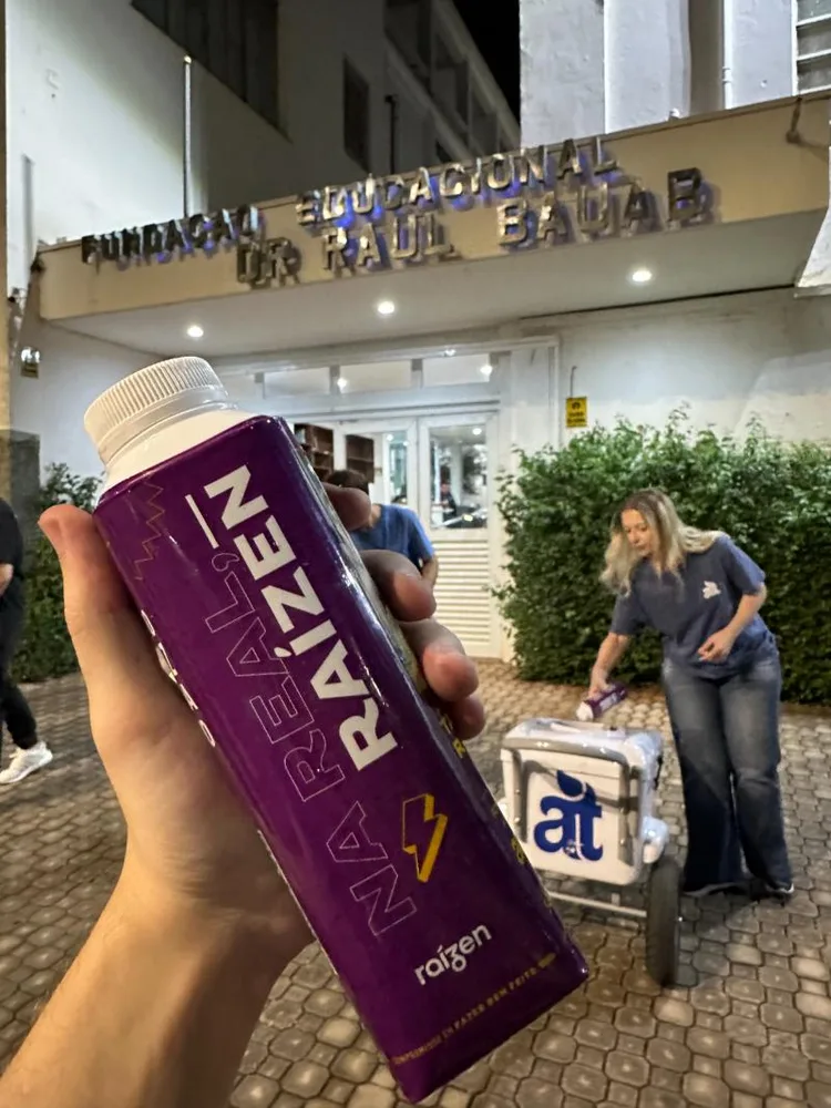 Caixinha roxa personalizada da Raízen e carrinho da Acqua.Tís em frente a uma universidade